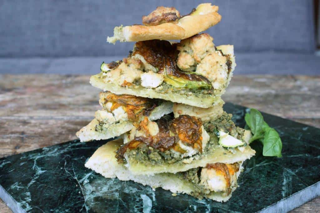 Preparing vegan pesto pizza with zucchini blossoms and cashew ricotta