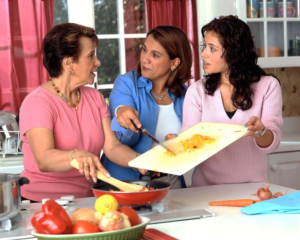 Three people cooking together, puutting chopped vegetables into skillet