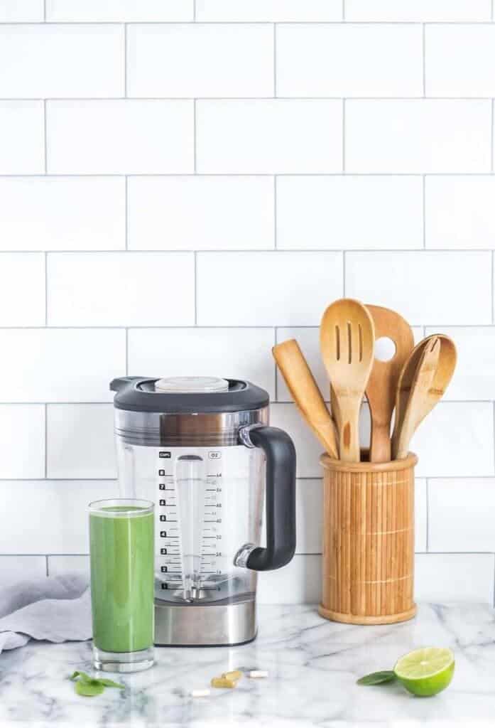 Blender, wooden spoons, glass containing green smoothie on a countertop