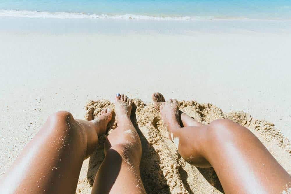 Two sets of legs in the sand in front of sea. guide to eco friendly vegan sunscreens
