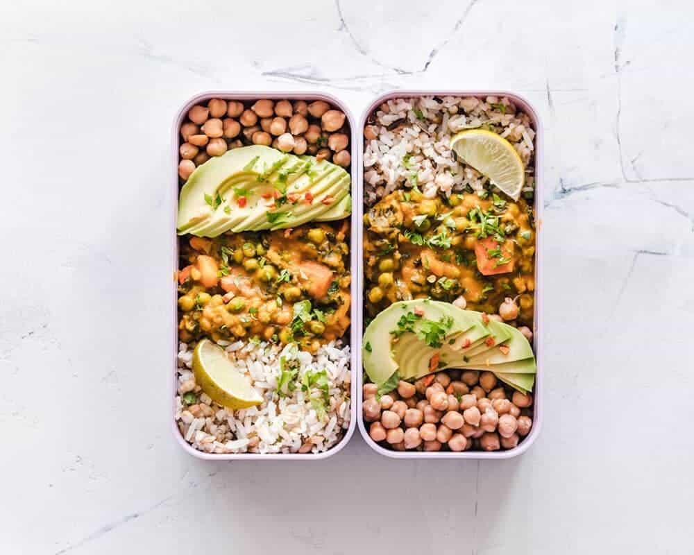 Two side by side tupperware containing vegetable curry, rice and chickpeas