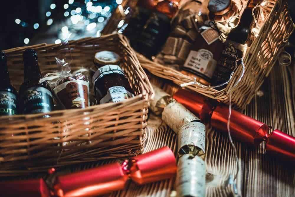 A wooden basket containing bottles beer and jars of spreads.