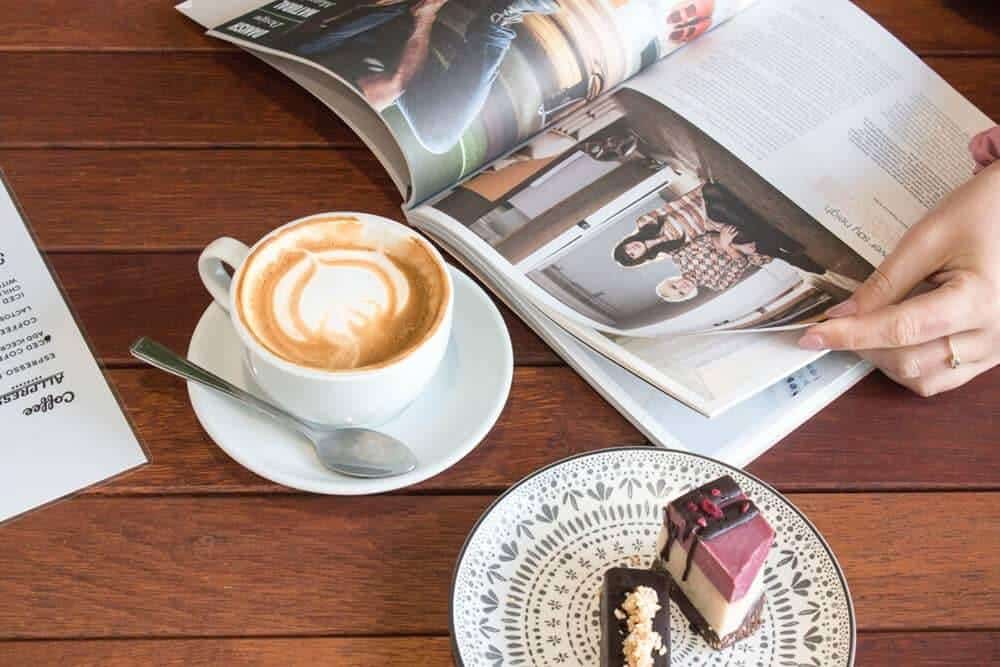 An open magazine, cup fo coffee and cake