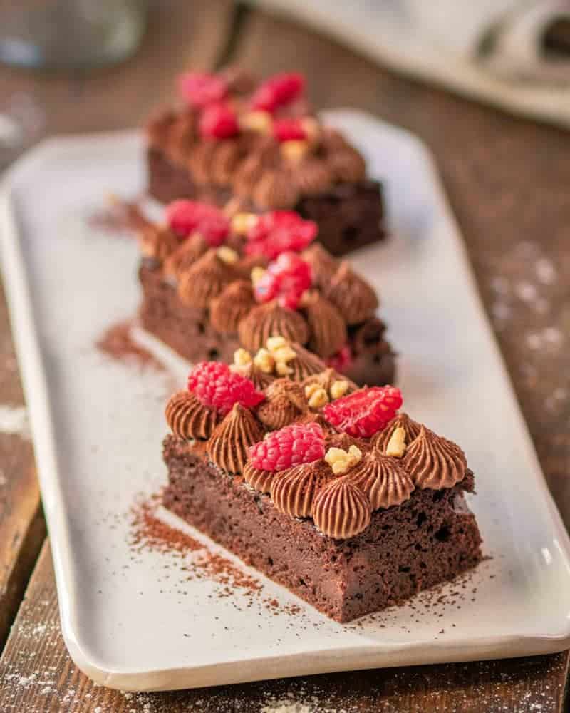 A tray of chocolate cakes with chocolate frosting, nuts and raspberries