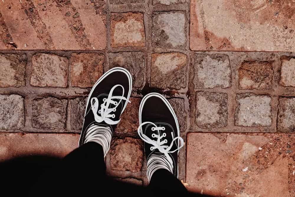 Person wearing black and white trainers standing on tiles