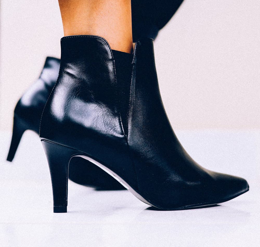 Person wearing stiletto heeled patent vegan leather black ankle boots