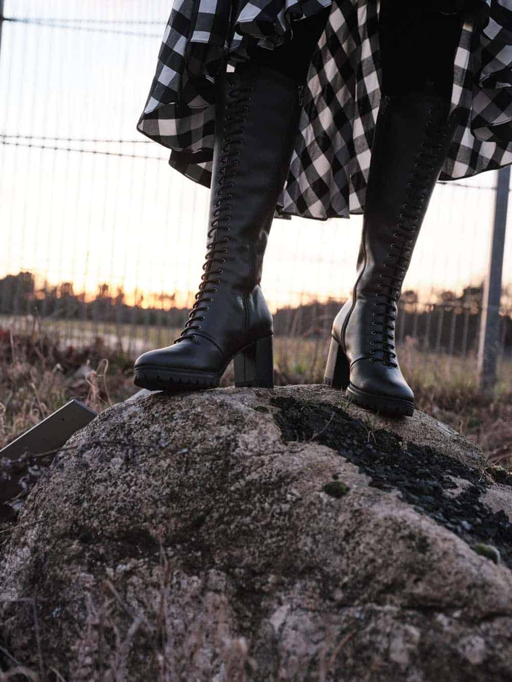 The legs and feet of someone wearing lace up knee high boots, standing on a rock