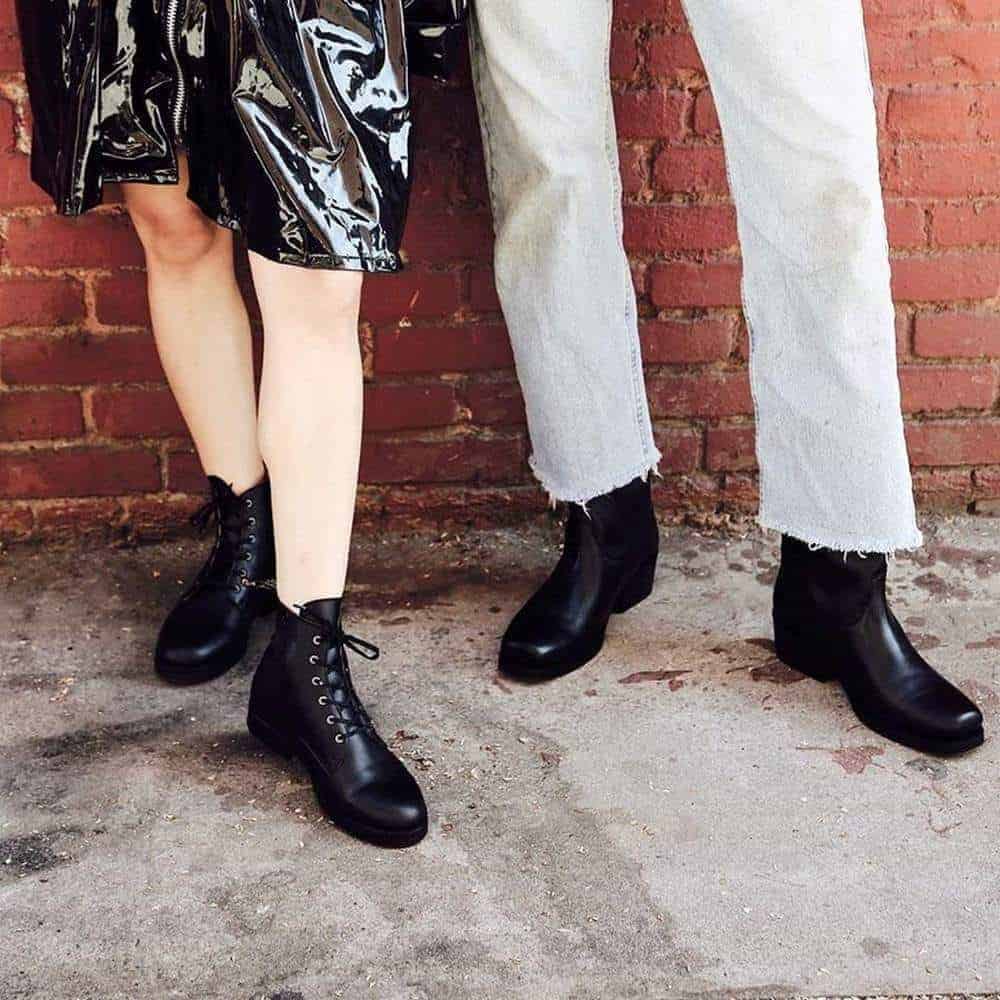 Two people standing, one wearing solid black vegan leather boots, the other wearing lace up black boots