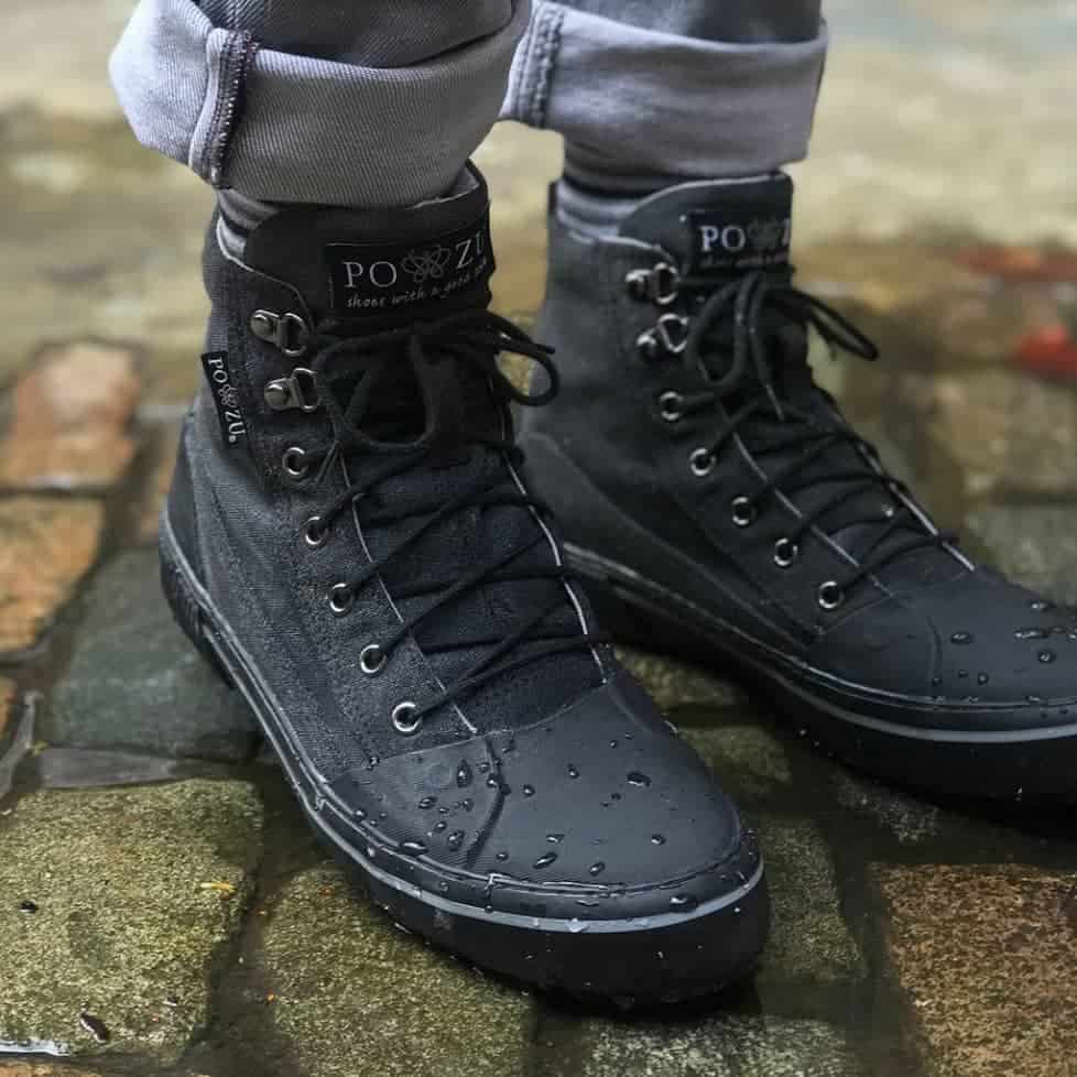 Black vegan boots lace up. Person is standing on wet ground with small water droplets on toe of boots