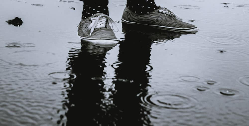 Feet wearing sneakers are partially submerged in a puddle