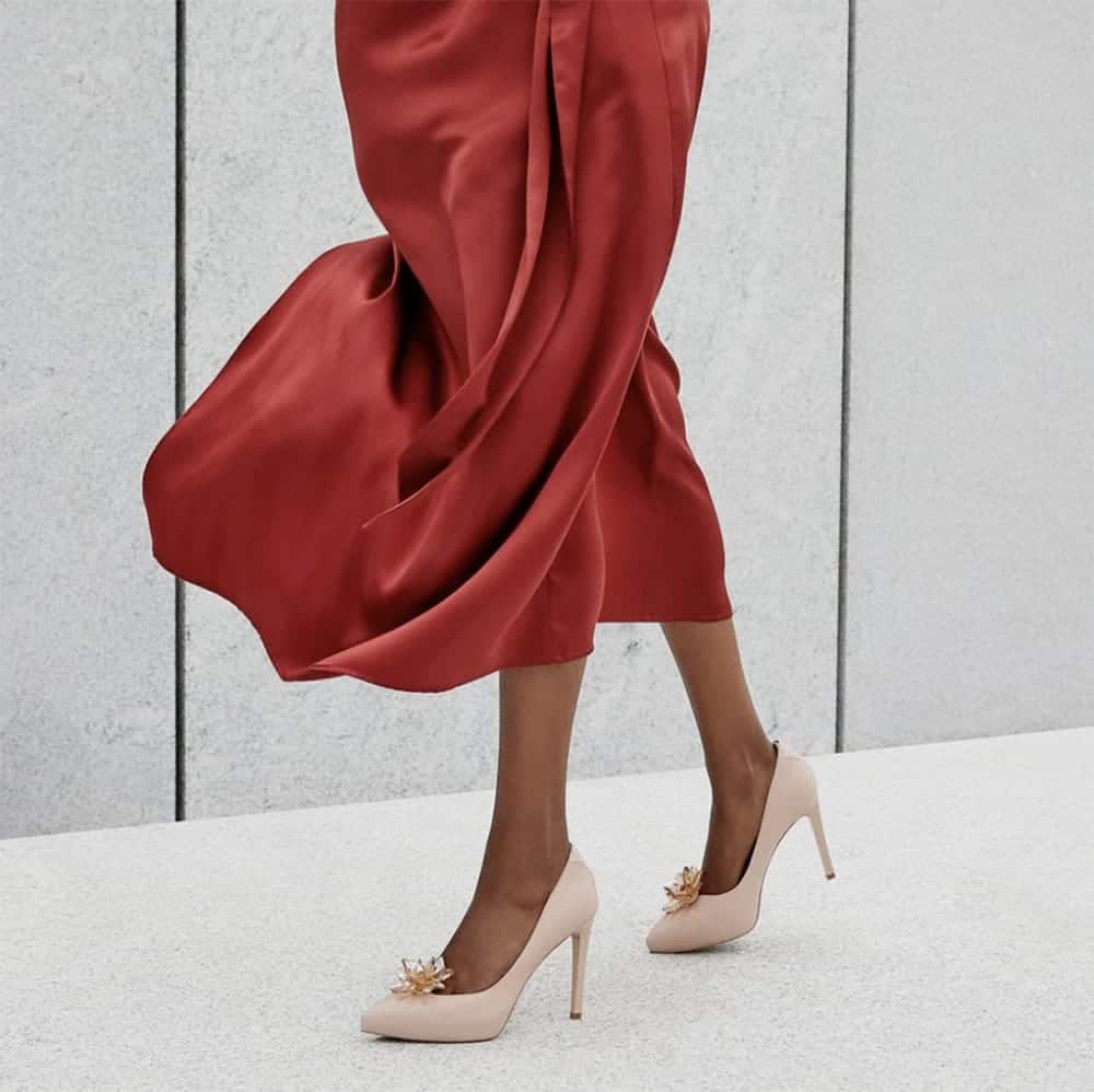 Person wearing beige stiletto heels and a long red skirt which is swishing