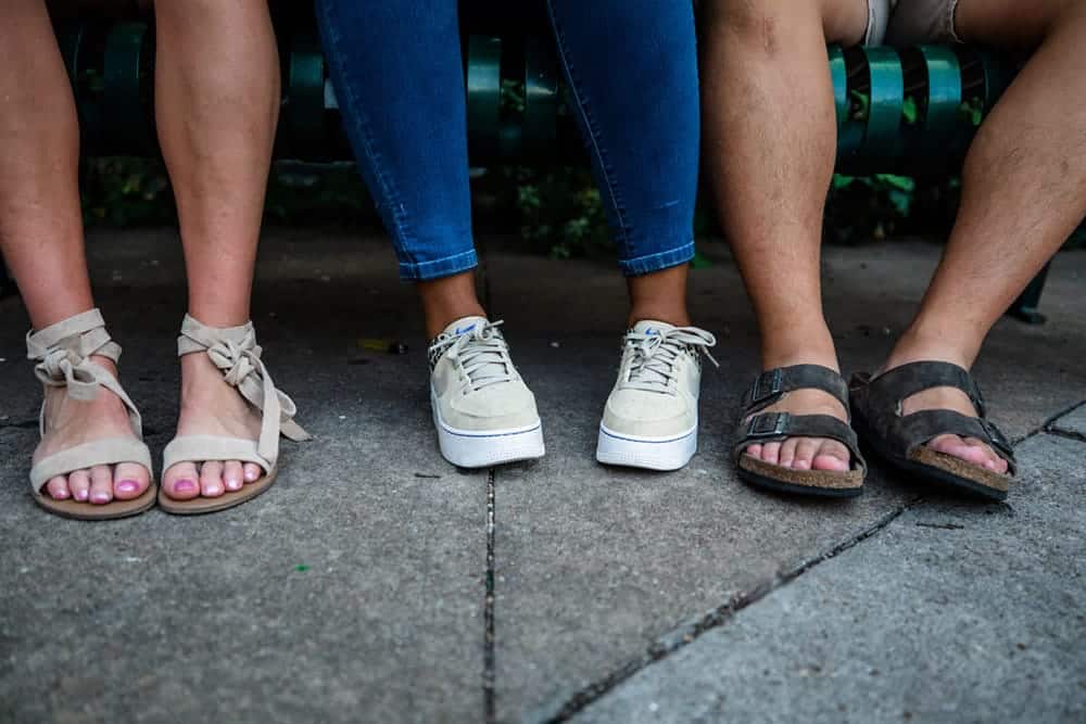 Three people's feet are shown, two wearing sandals and one wearing sneakers