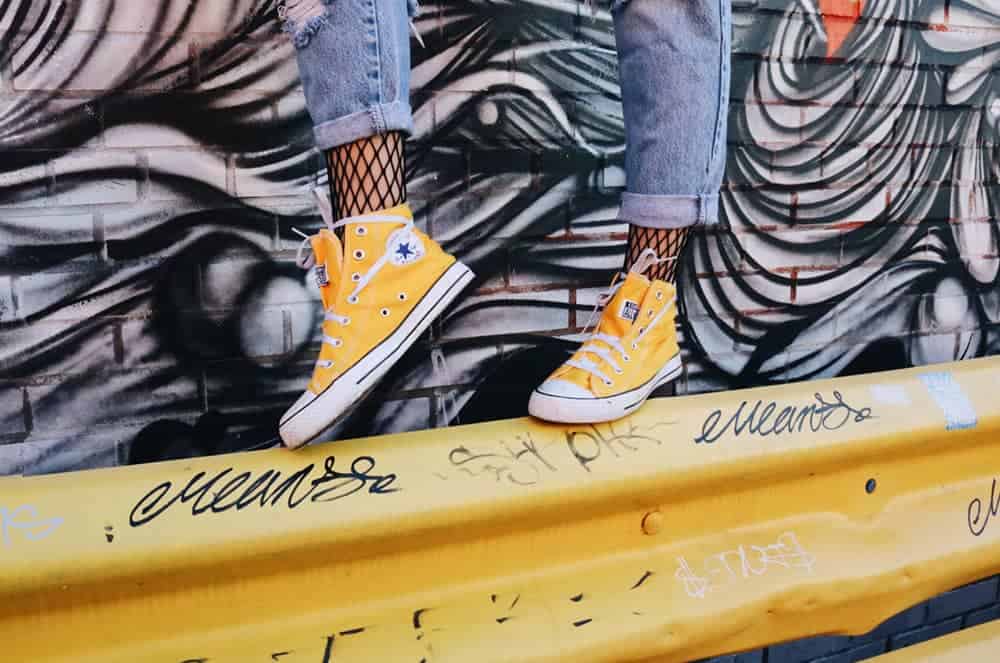 Person wearing yellow sneakers balances on yellow railing, only feet and lower calves are visible