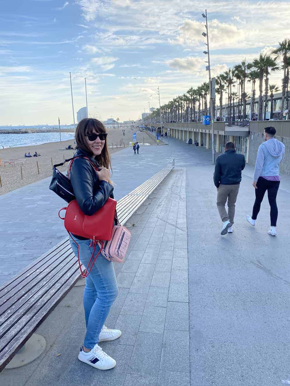 Blog author wearing three Doshi bags: pink camera bag, red backpack and black belt bag in front of beach