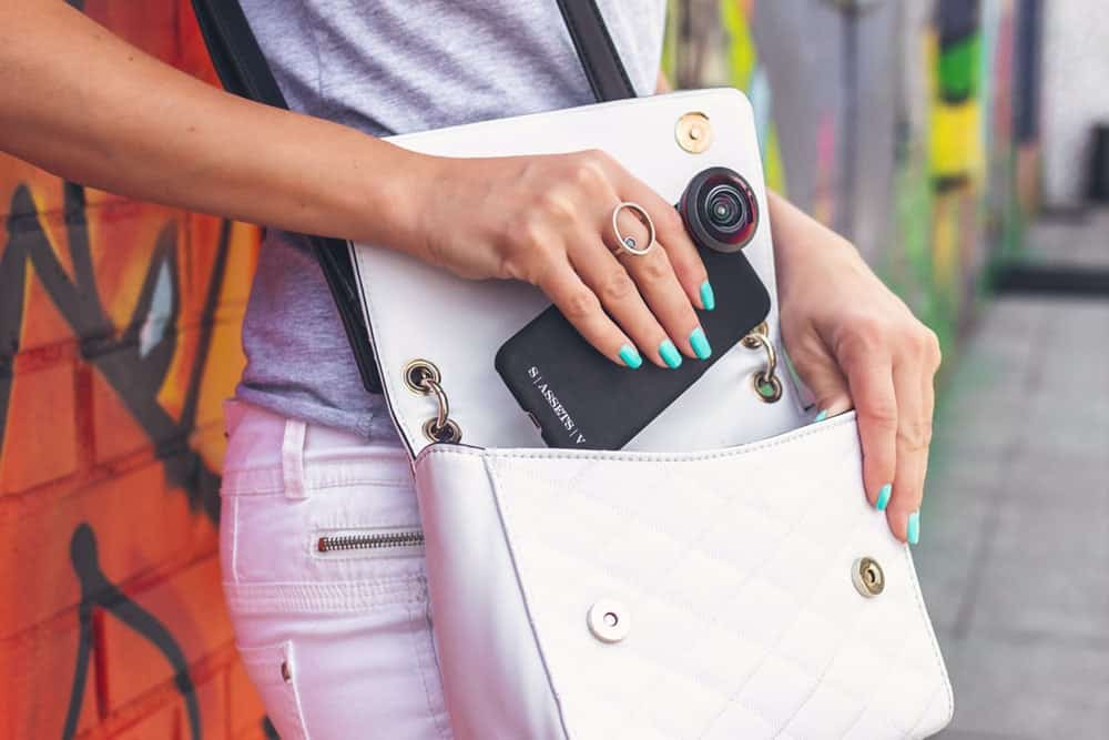 Woman placing phone into white crossbody bag
