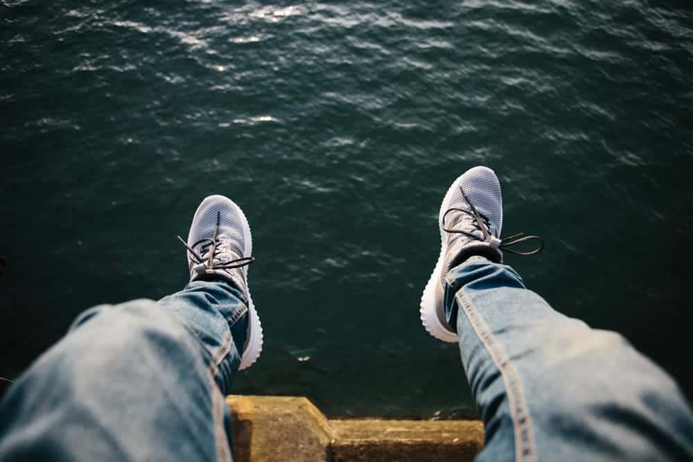 Photo taken from the perspective of someone sitting with their legs hanging over a body of water, showing their jeans and sneaker