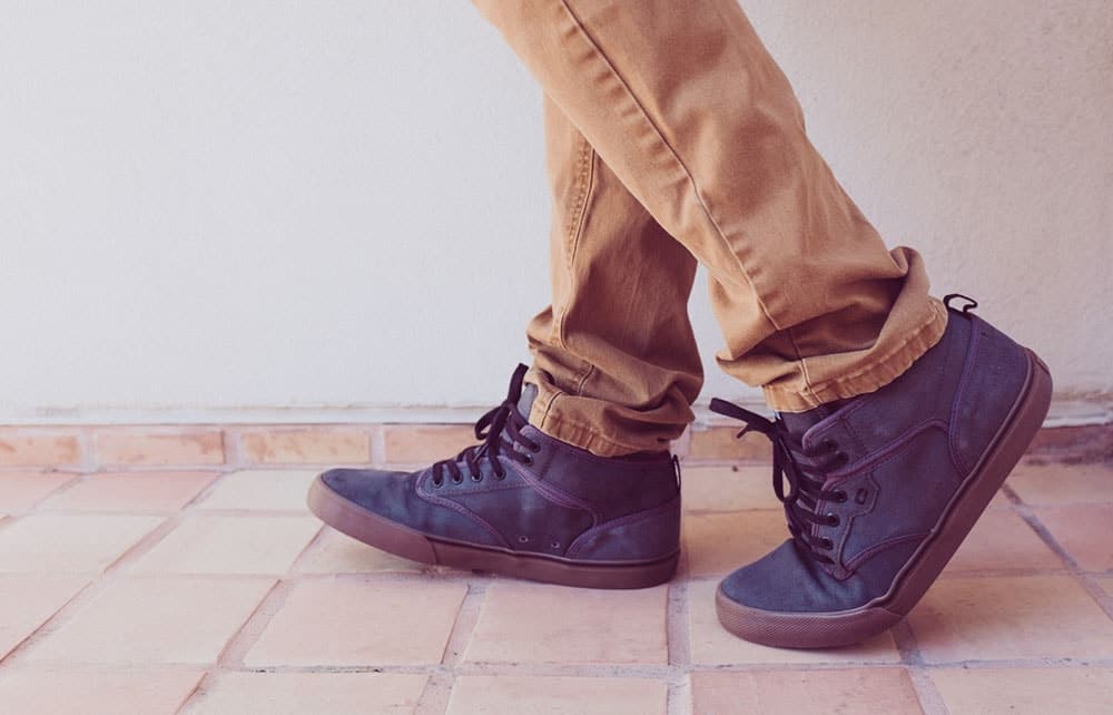 Feet shown walking across tiles in dark blue trainers