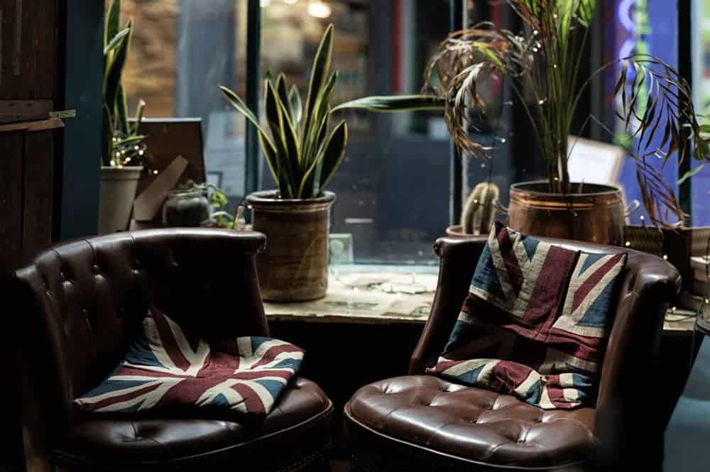 Two dark brown leather chairs with Union Jack cushions and platns behind them