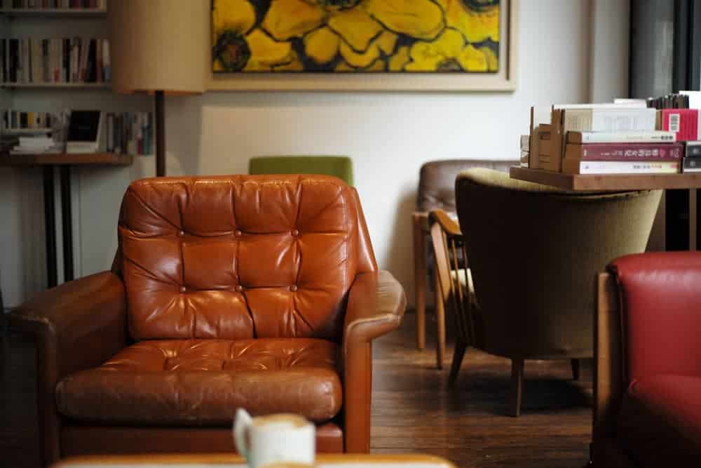 Brown leather chair with a table and a mug of coffee in front of it, plus more chairs and tables plus books behind it