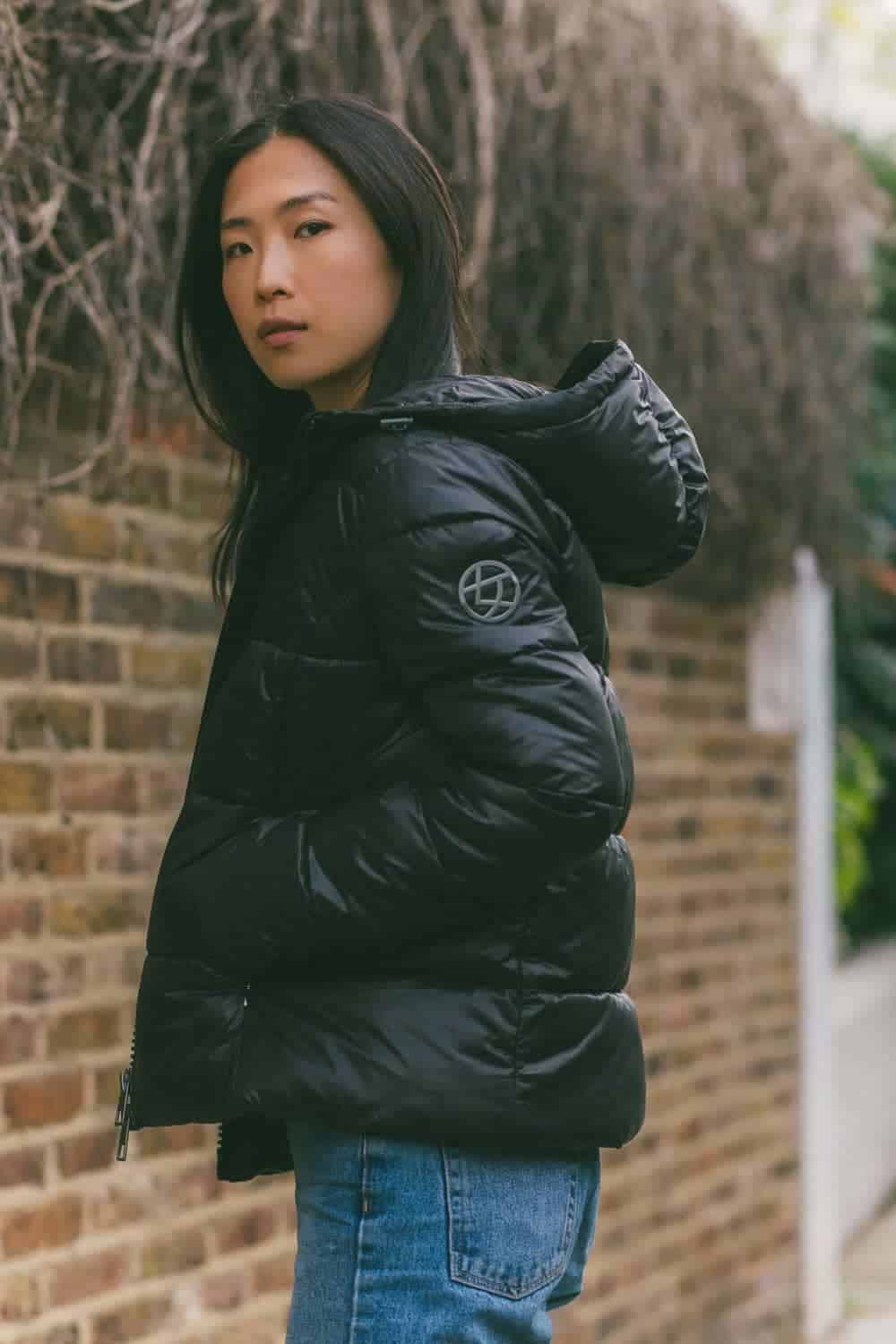 Person wearing black puffer jacket and jeans standing in front of brick wall