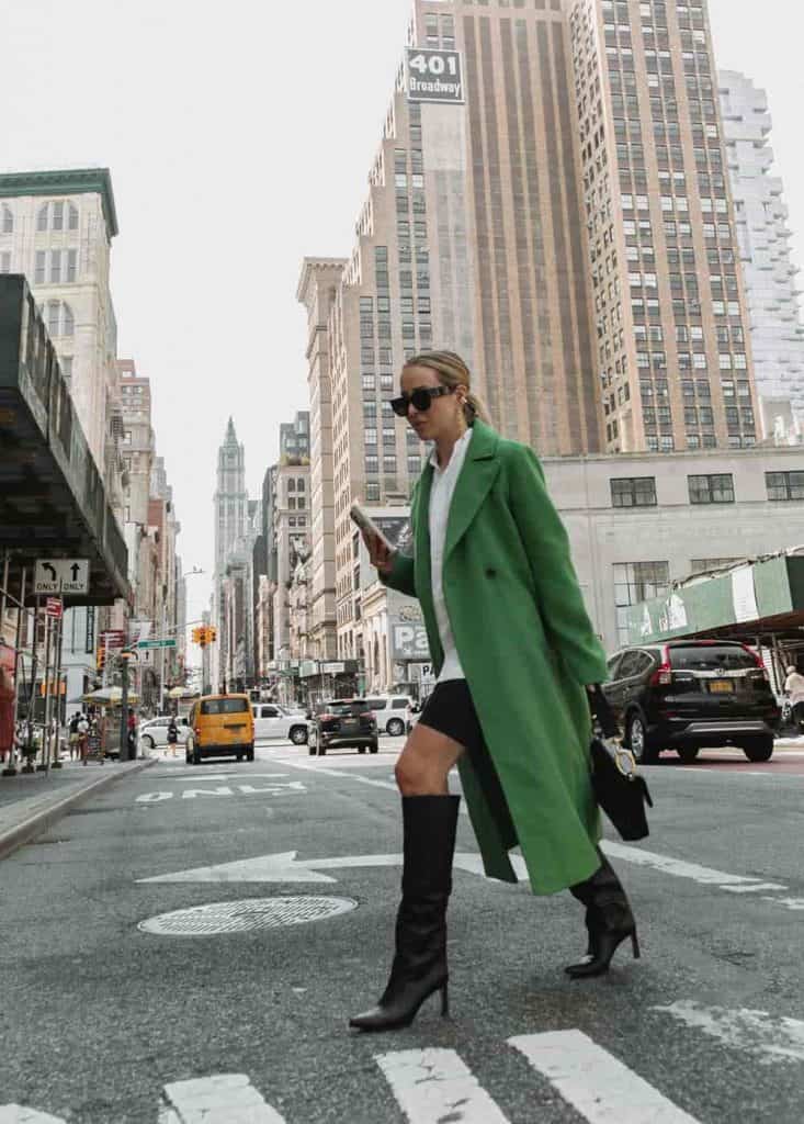 Woman wearing green long vegan wool coat crossing the street in a city