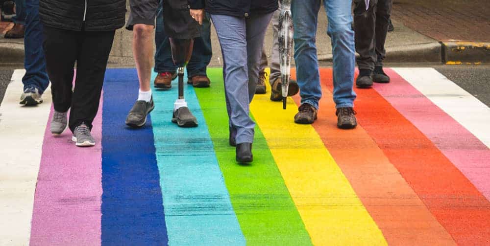 Feet of people shown crossing street painted with rainbow stripes