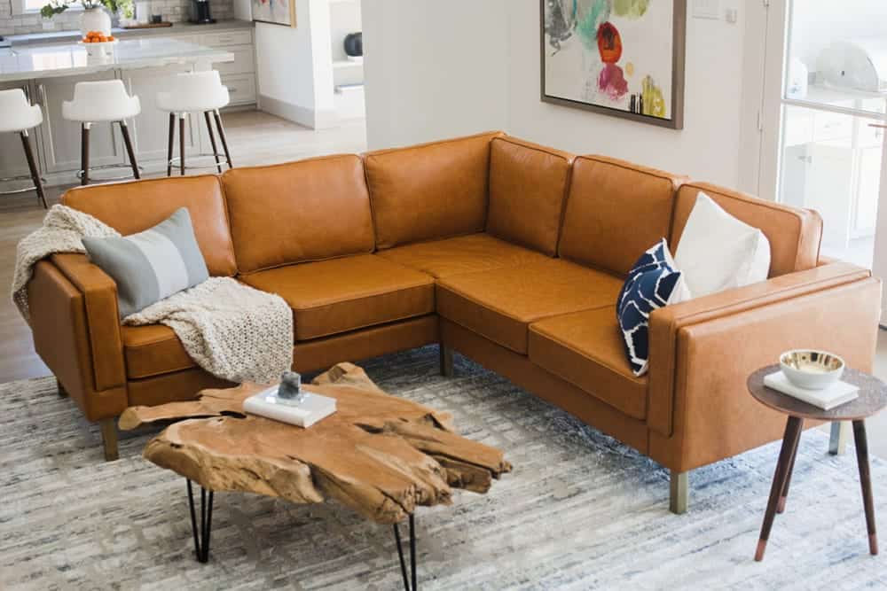 Corner sectional brown vegan leather sofa pictured in living room with cushions, blankets and driftwood table