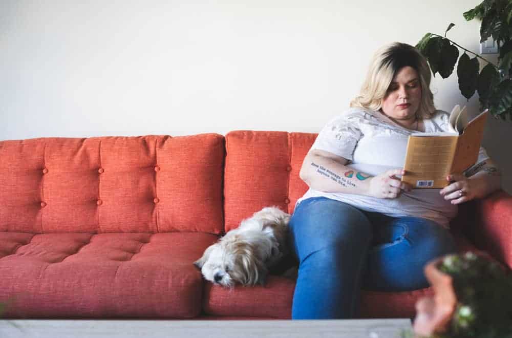 Person reading a book on the sofa with dog sat next to them