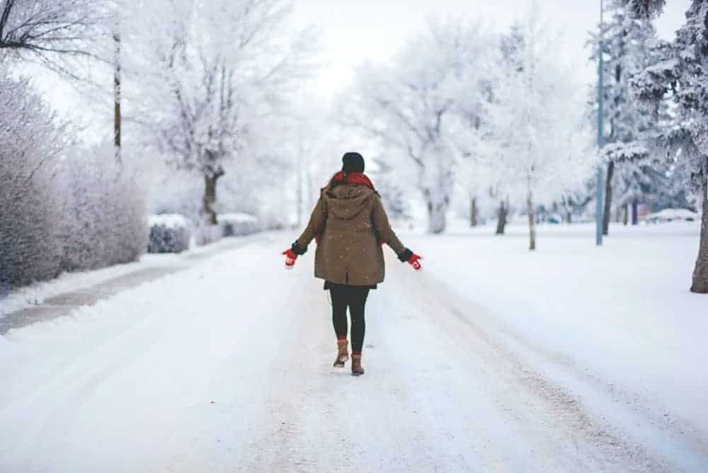 Person walking down snowy street in coat and boots