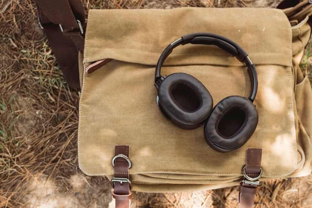 Light brown canvas messenger bag with headphones on it lying on grass