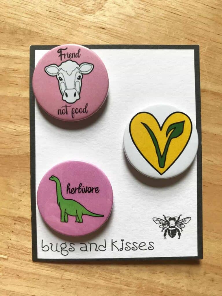 Vegan badge set. One has vegan symbol, another a cartoon dinosaur which reads "herbivore" and another a cartoon cow which says "friend not food"