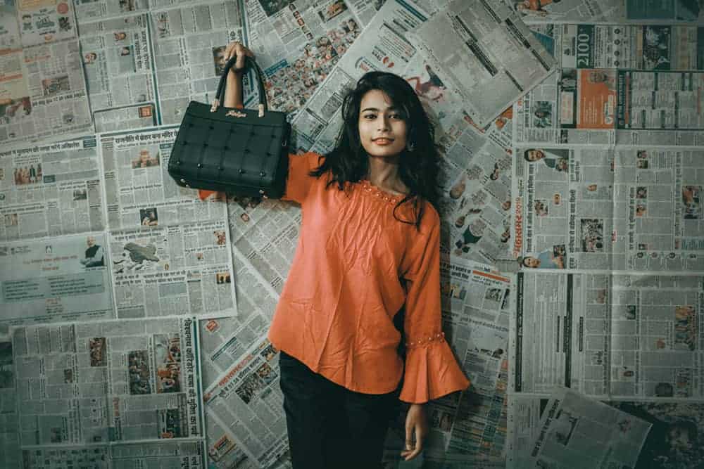 Person holding up black bucket bag in front of wall covered in newspapers