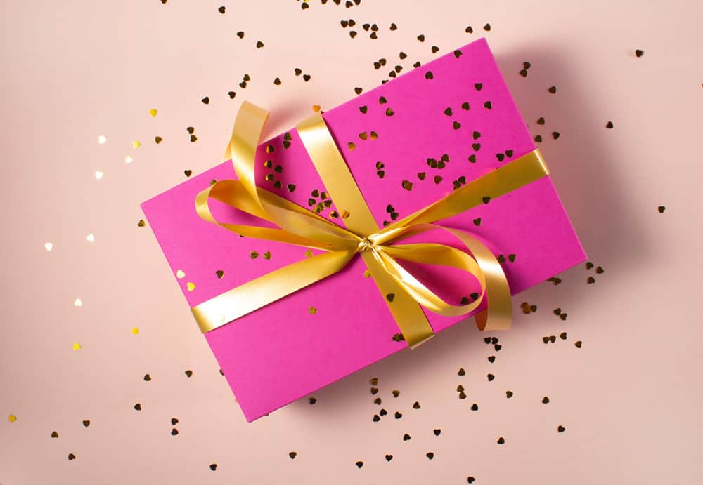 Vegan gifts UK: present wrapped in fuschia wrapping paper on salmon background with gold ribbon and gold glitter