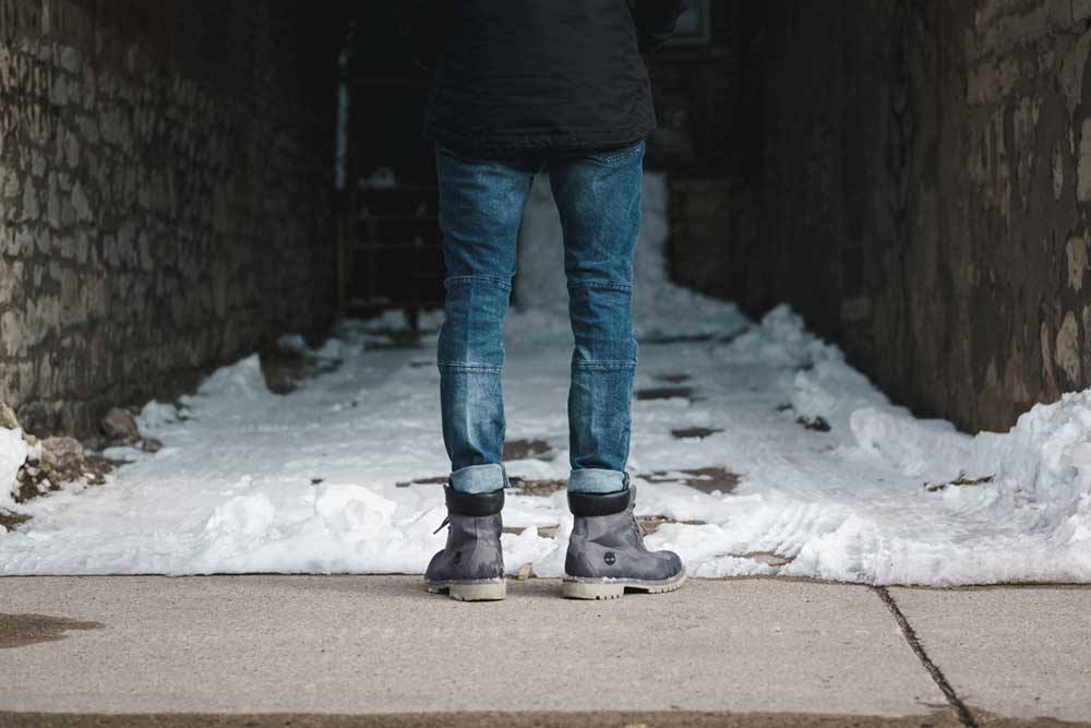Person wearing boots and jeans standing in front of snow covered path