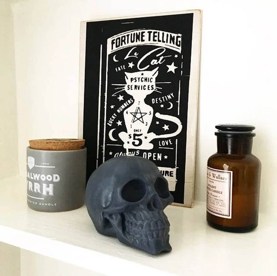 Black skull vegan candle on shelf in front of apoethcary jar and fortune telling poster