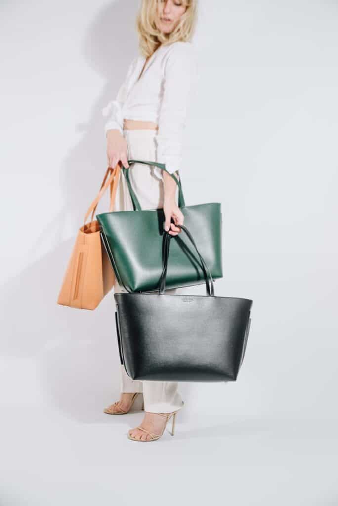Woman holding three vegan leather Luxtra tote bags in camel, green and black