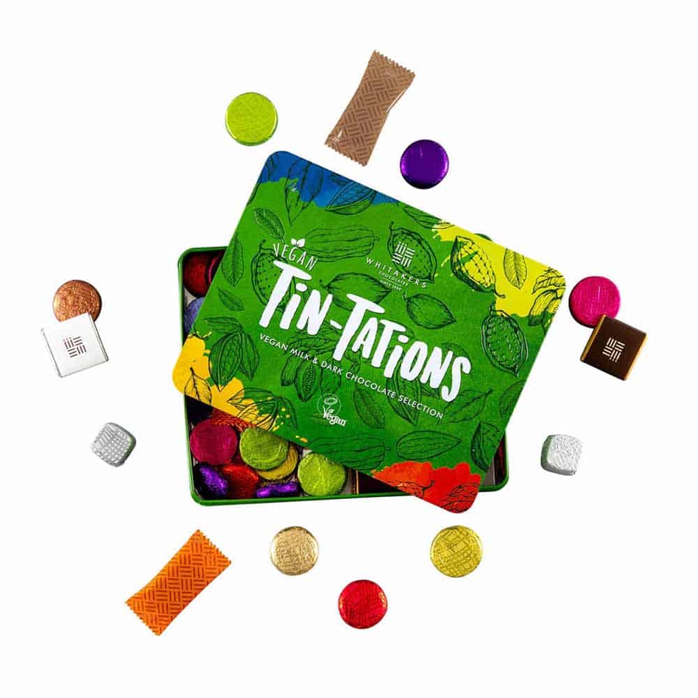 Vegan Quality Street style chocolate. Green tin that says "Tin Tations" open and surrounded by differently-coloured and shaped vegan chocolates