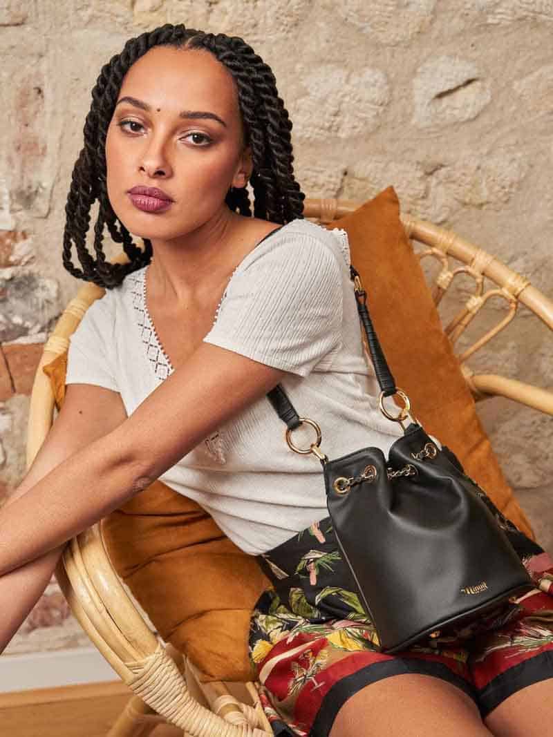 Person holding black vegan leather bucket bag with gold hardware