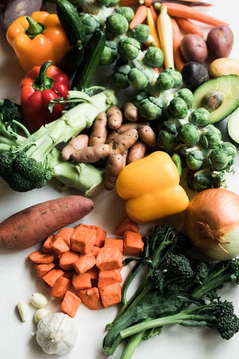 Pile of vegetables including potatoes, diced sweet potato, greens, brussels sprouts, onion, broccoli, red and yellow pepper