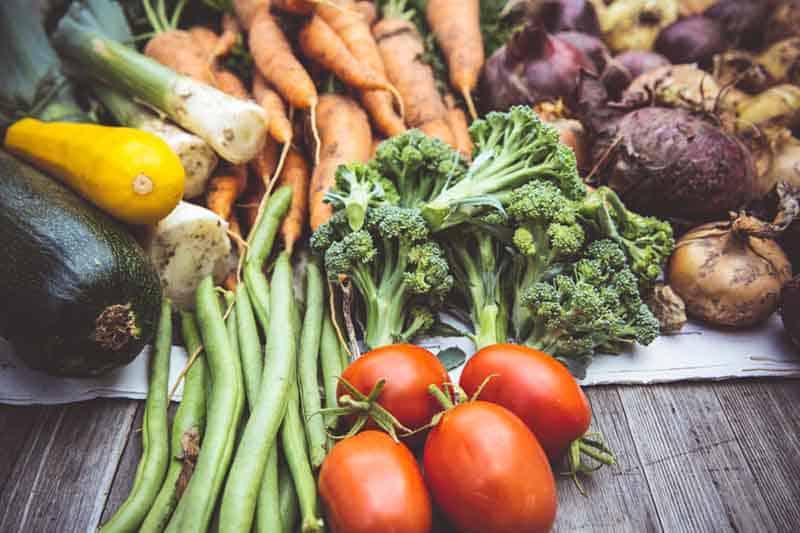 Pile of fresh vegetables including tomatoes, broccoli, carrots, green beans, squash and mixed root vegetables