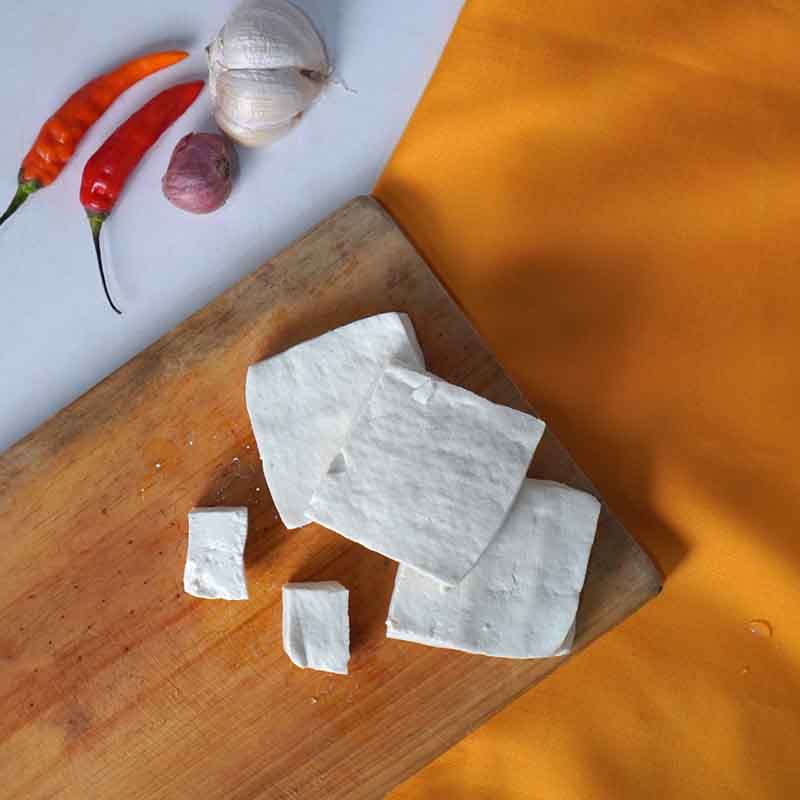 Chopping board with several blocks of tofu, and garlic and chillies on one side