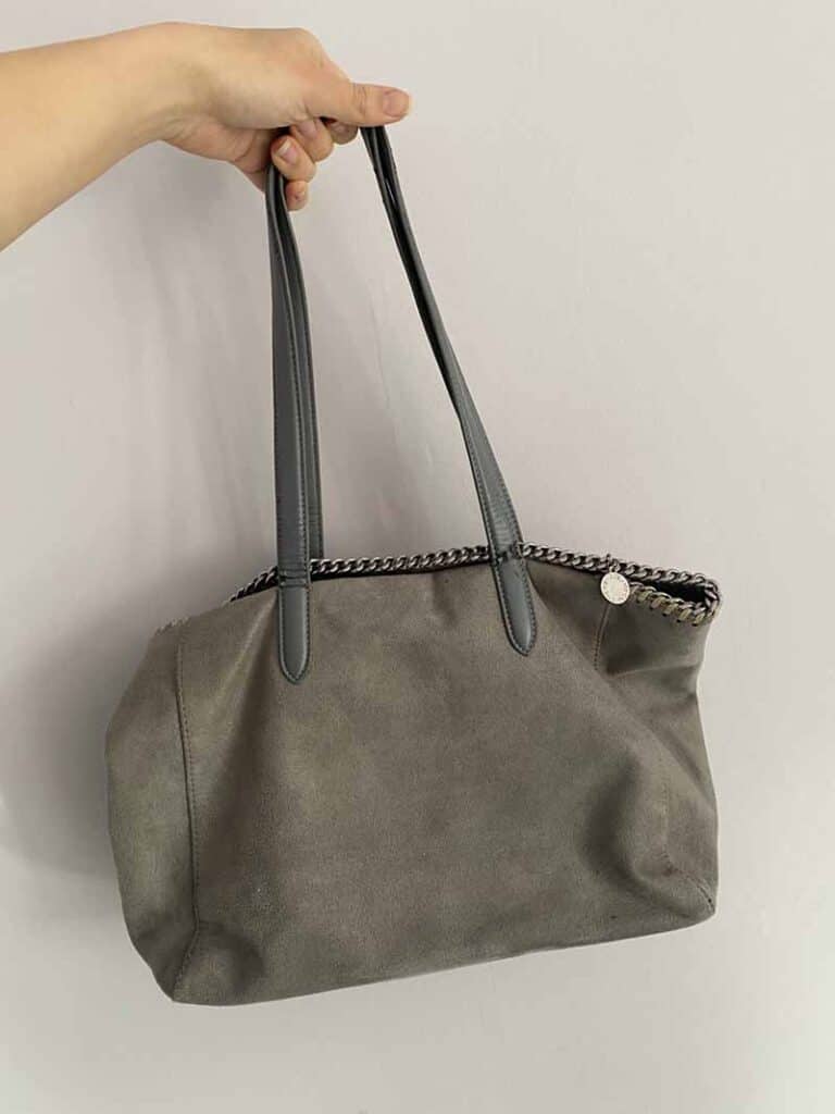 Author holding Stella McCartney tote bag (grey vegan leather with signature chain trim)