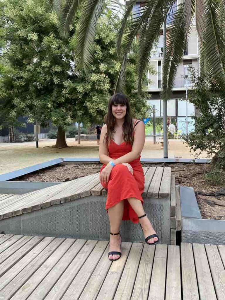 Author (Caitlin Galer-Unti) shown sitting in a park in Barcelona wearing red dress and Veerah Dian sandals